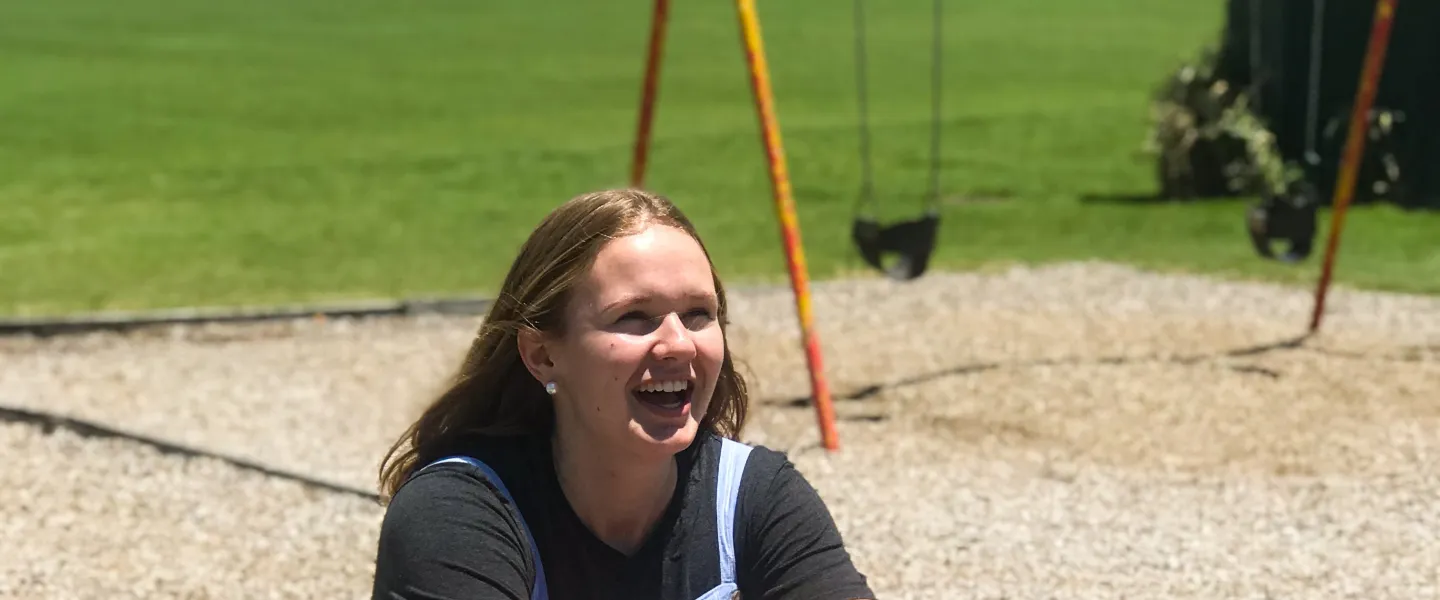 Smiling teenage girl sitting on a teeter totter outside on a playground