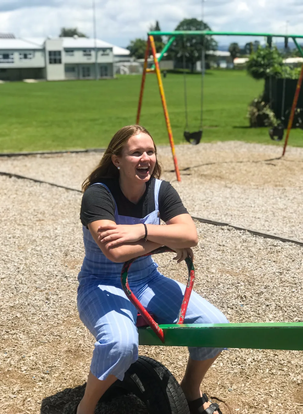 Smiling teenage girl sitting on a teeter totter outside on a playground