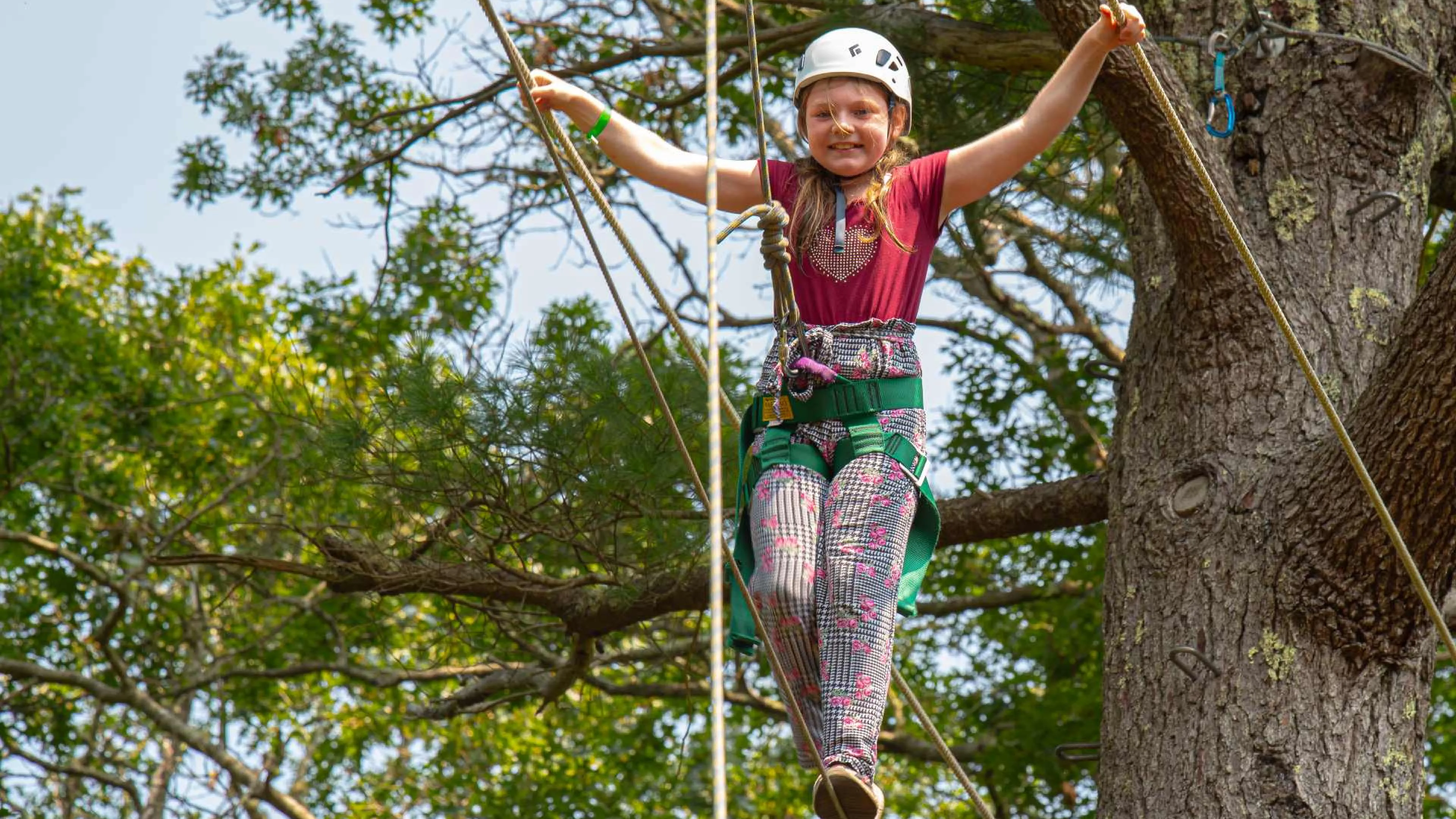 Smiling girl wearing a helmet walking the ropes at Camp Clarks ropes course