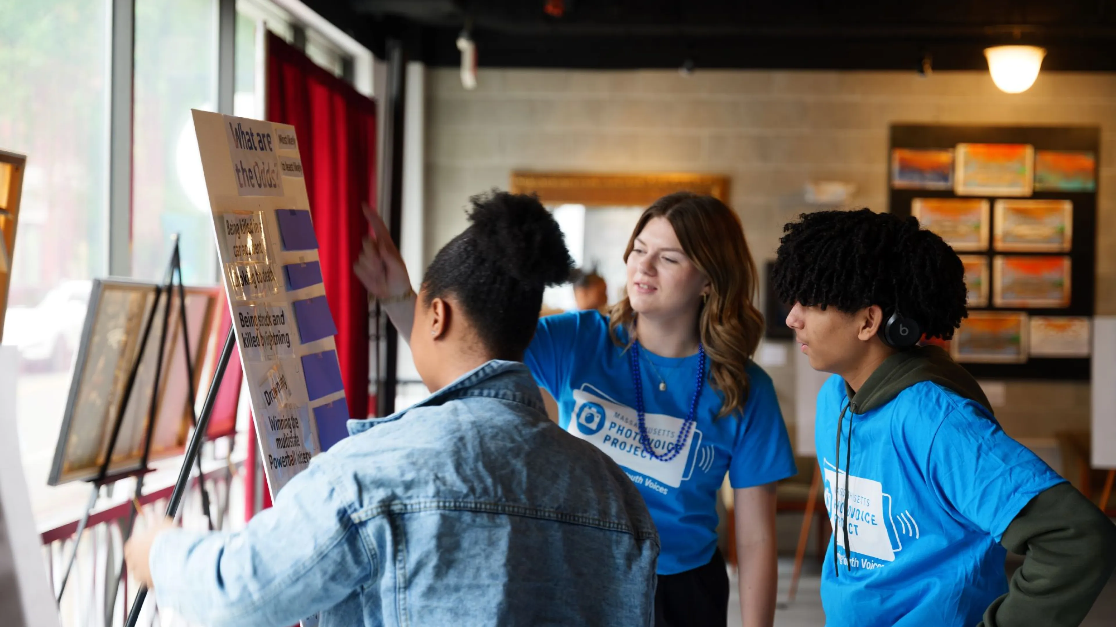Teens looking as a poster, "What are the Odds" on display at a photo voice event