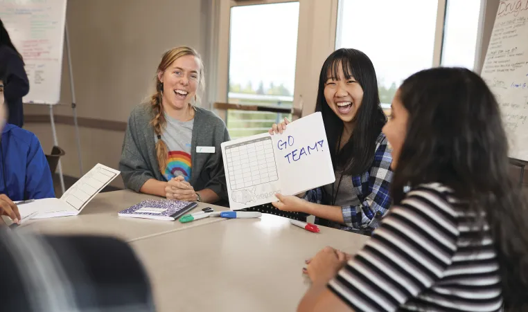 Group of young ladies sitting around a table showing off their notebook with "GO TEAM!" written