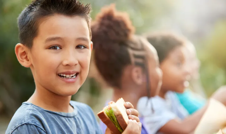 Boy eating sandwich outside with other children at summer camp