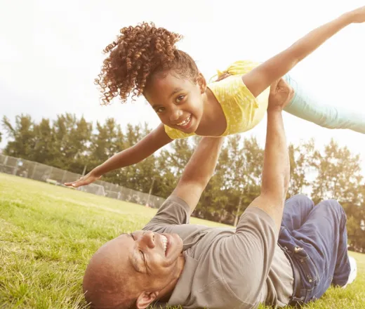 Dad lying on grass holding child up in his arms as they both smile having fun