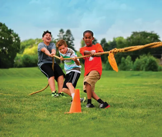 Three boys pulling a rope while playing tug of war in a grassy field