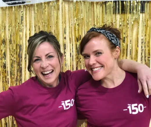 Two young women smiling at the camera wearing their 150 Club shirts