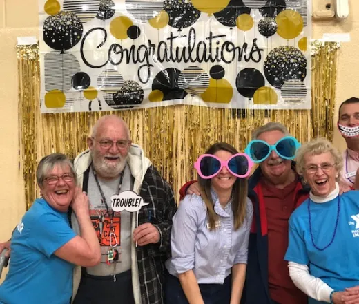Group of 150 Club participants and staff standing in front of a congratulations banner
