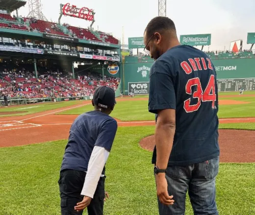 Kid with a Red Sox hat and shirt on the field with their mentor at Fenway - Mentoring